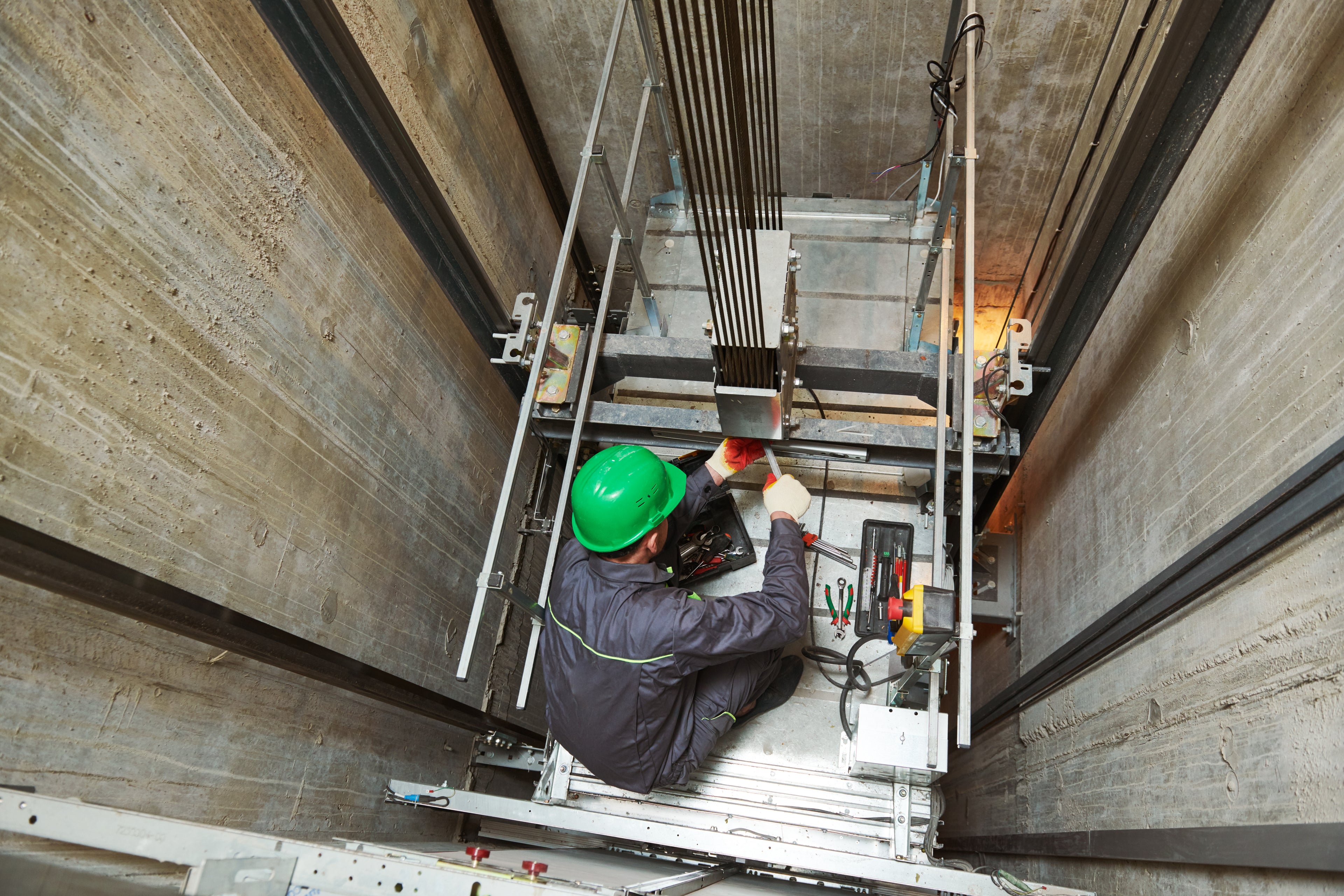 Person in a green helmet working inside an elevator shaft.